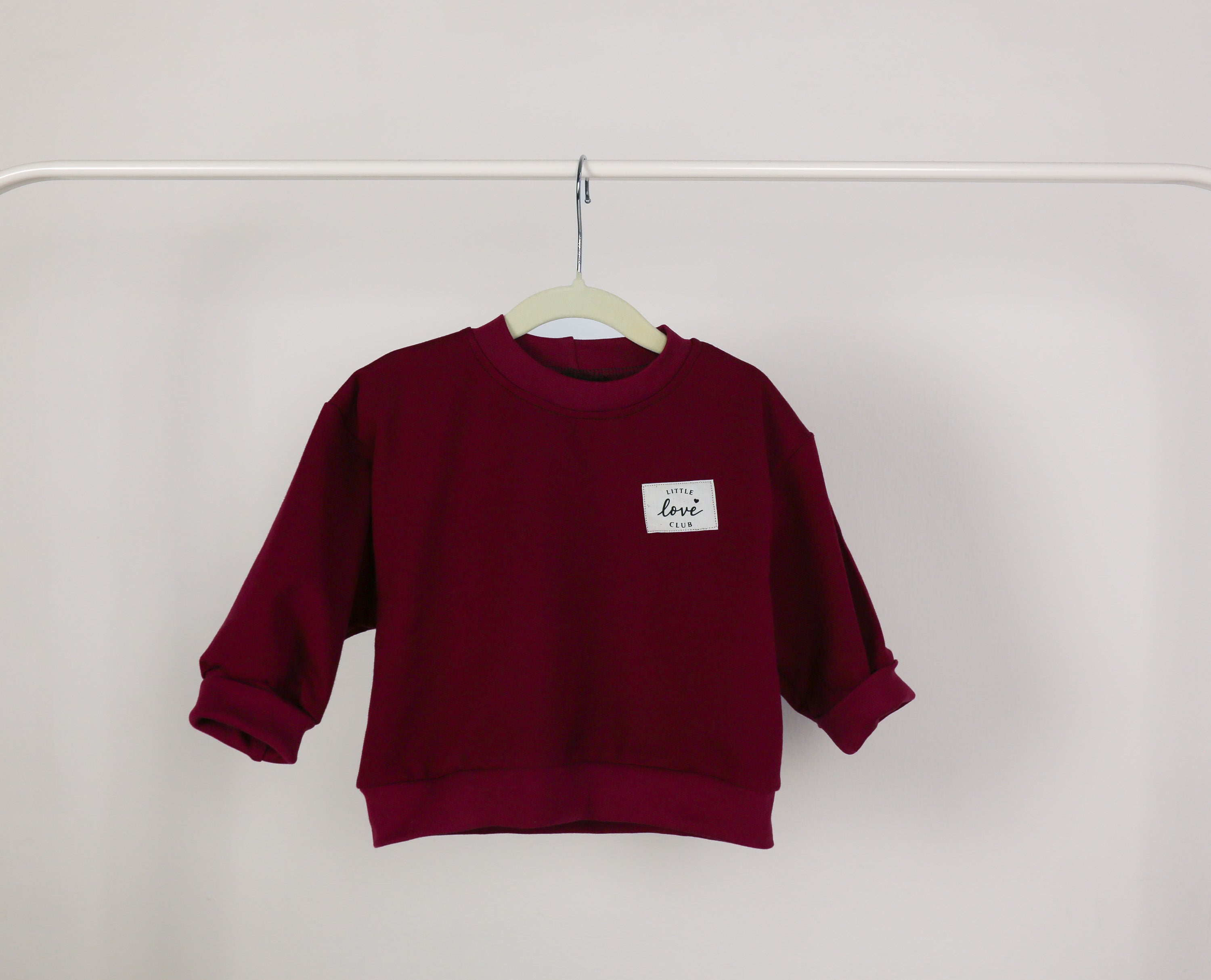 Detailansicht „Love Club“-Patch auf dunkelrotem Sweatshirt
