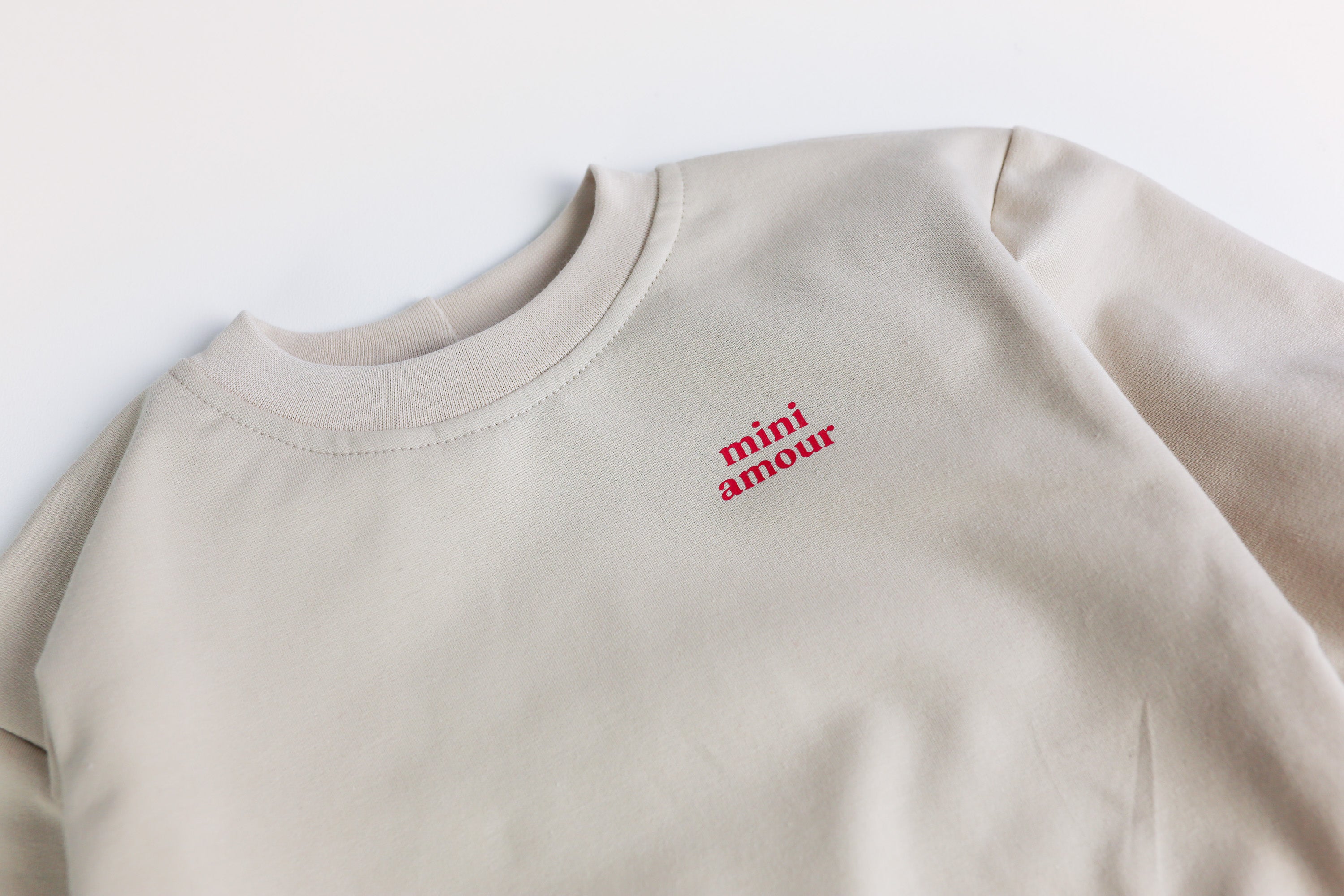 Detailansicht Mini Amour Schriftzug auf beigem Sweatshirt
