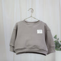 Taupefarbener Oversize-Strickpullover für Babys und Kinder mit überschnittenen Schultern und Cozy-Club-Detail
