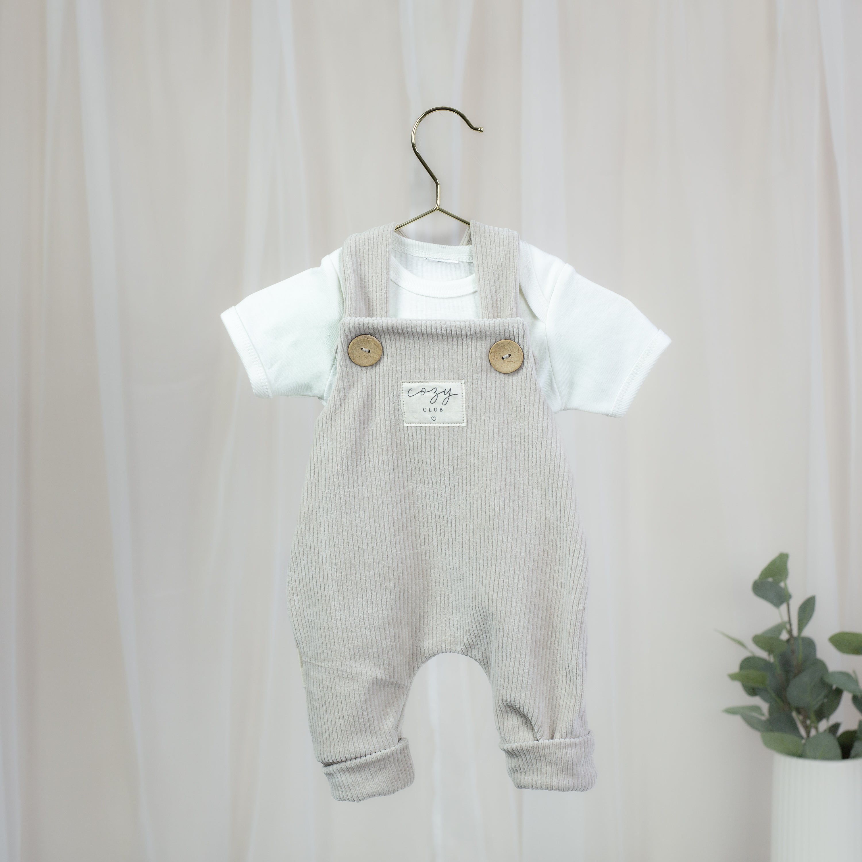 Elastische Cord-Latzhose in Sandbeige für Babys mit Holzknöpfen und Cozy-Club-Patch
