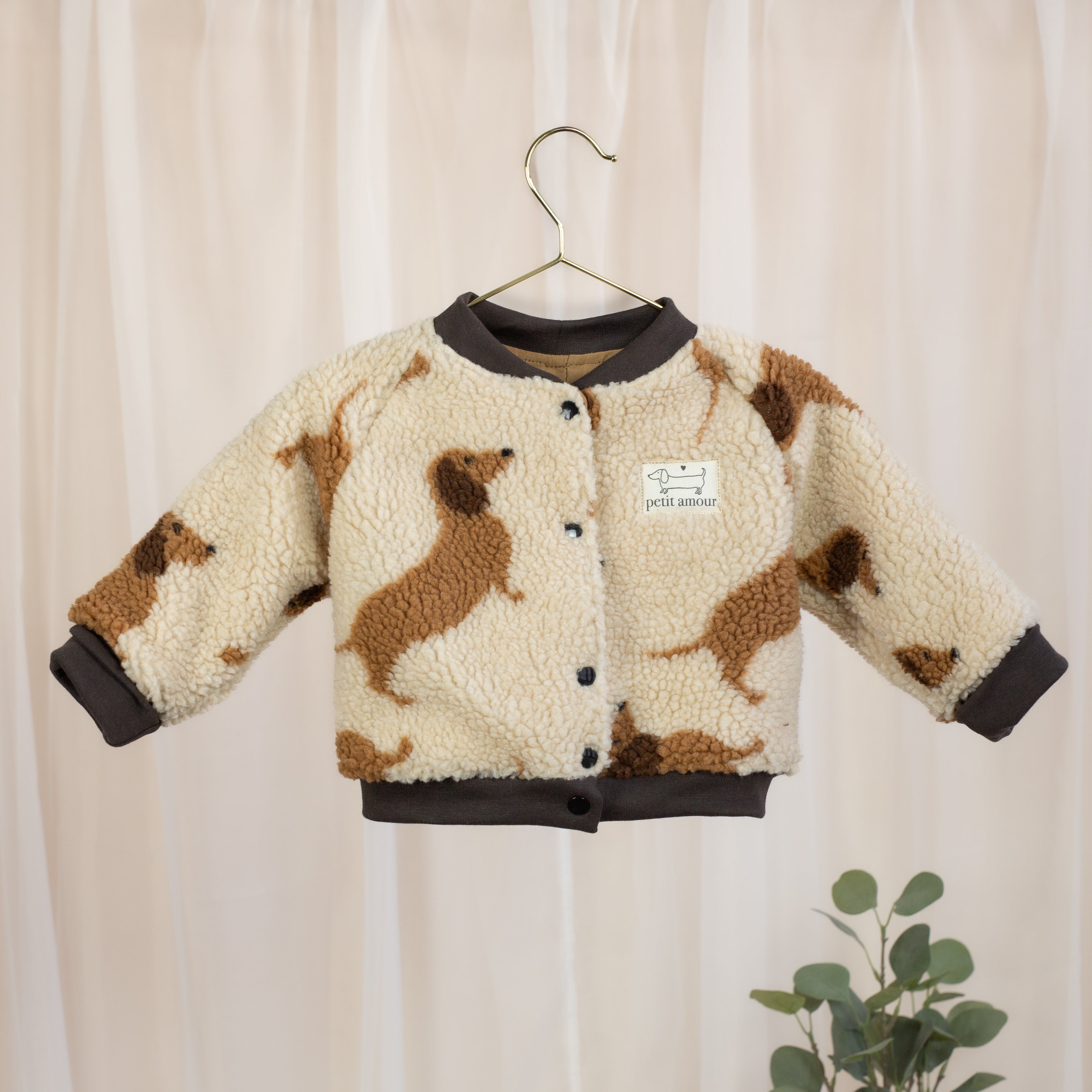 VOODULU Teddy-Collegejacke in Creme mit braunen Dackelmotiven, dunklen Bündchen und Petit-Amour-Label, Vorderansicht.